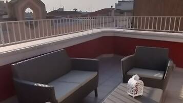 Una terraza en la azotea con muebles de mimbre y un farol blanco.
