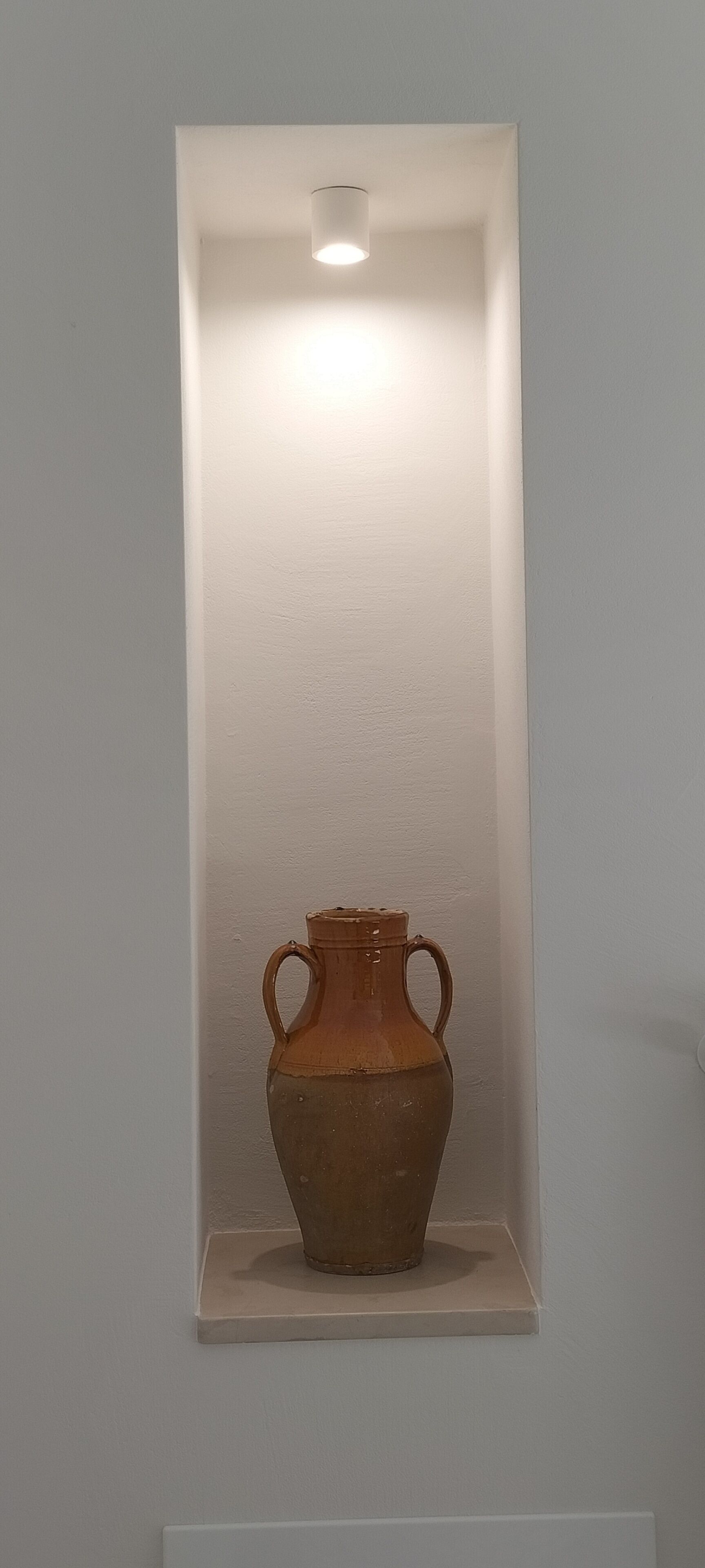 A ceramic vase with two handles in a white shelf against a plain wall.