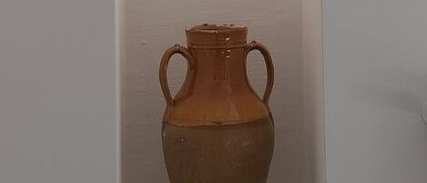 A ceramic vase with two handles in a white shelf against a plain wall.