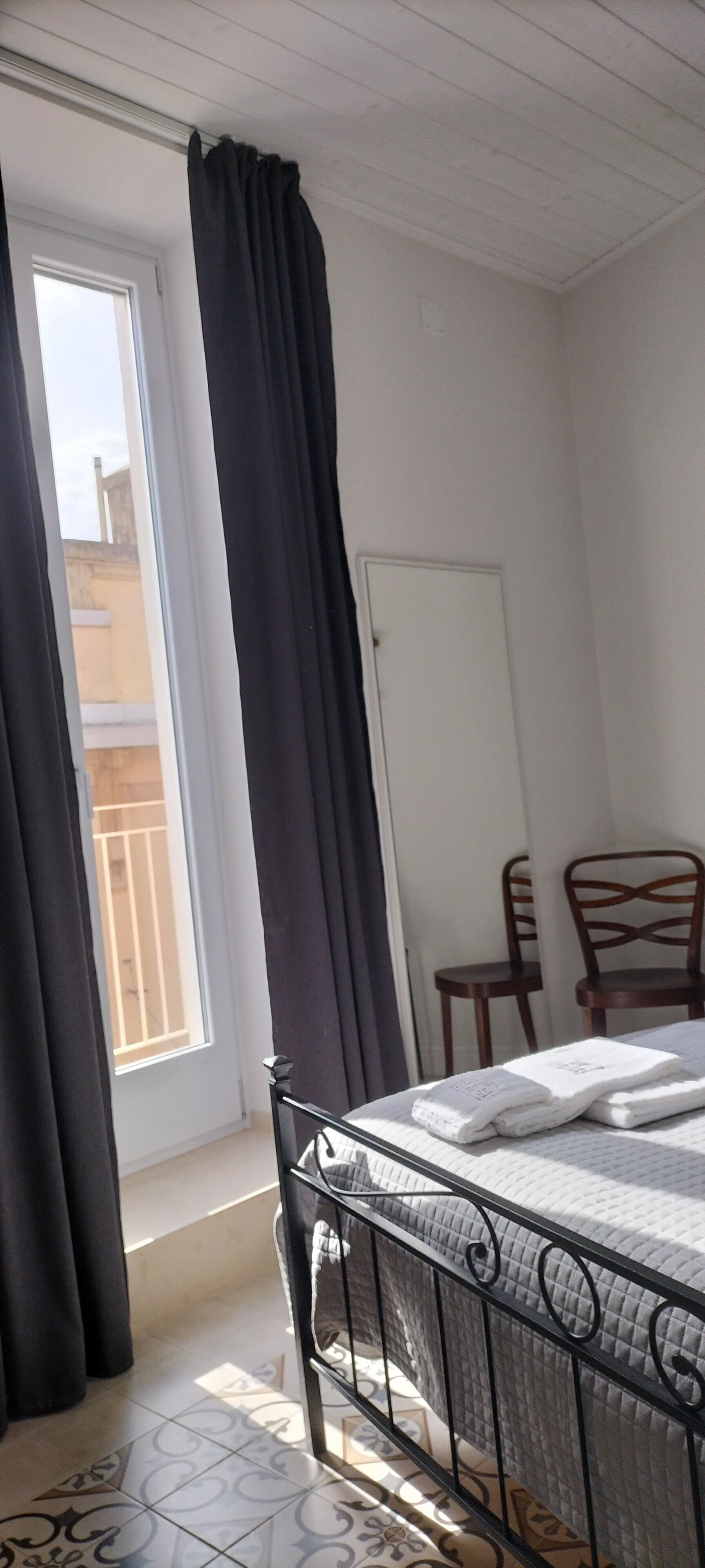 A bedroom with a bed, a window with curtains, a door, and two chairs.