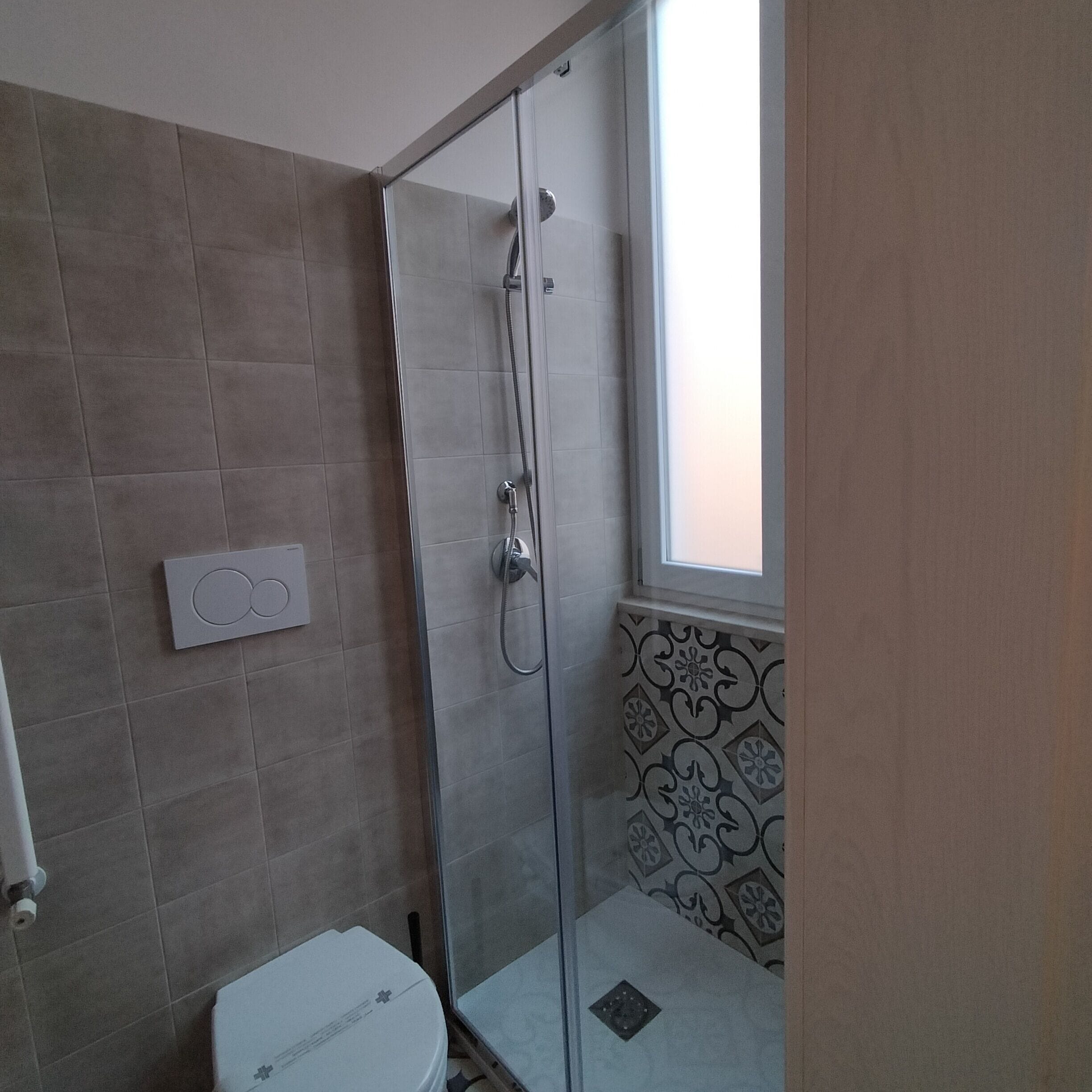 Ein modernes Badezimmer mit Duschkabine aus Glas, Toilette und Fenster für natürliches Licht.