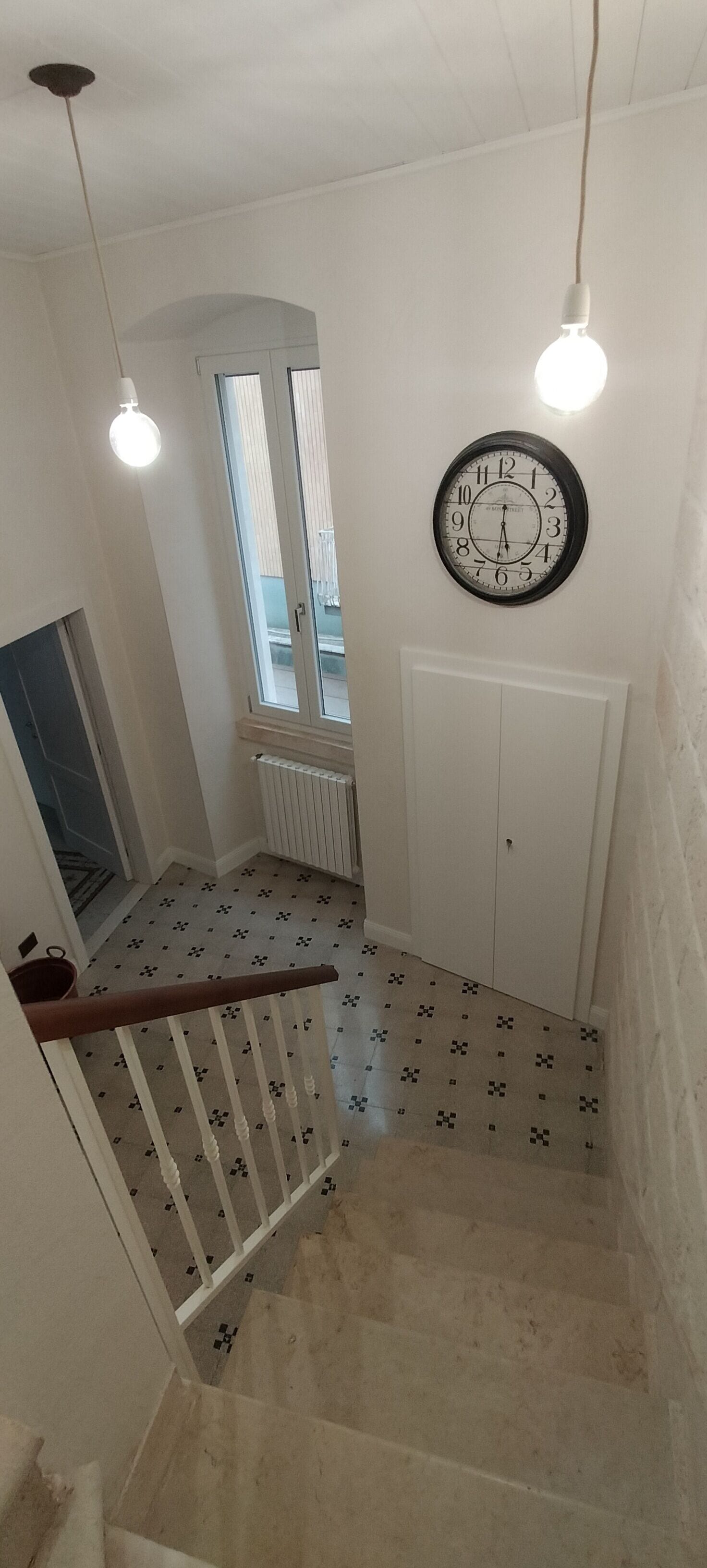 A staircase with patterned tiles, a white door, and a wall-mounted clock.
