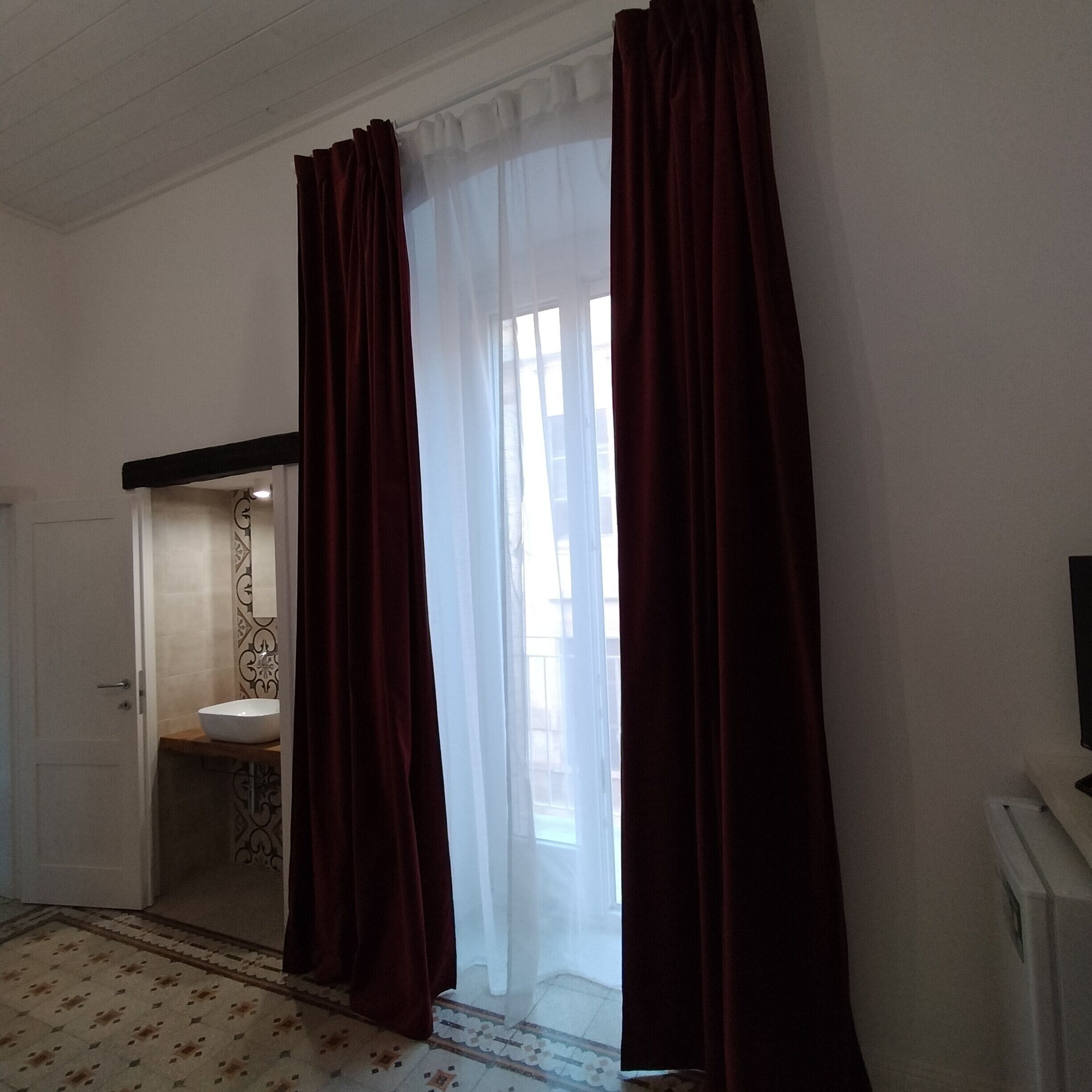 Une pièce avec une salle de bain, une porte et une fenêtre avec des rideaux.