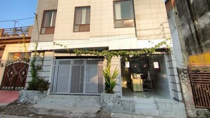 A multi-story building with a tiled facade, a gated entrance, and a small garden area with plants. - Hotel Nue-Nest (Rishikesh)