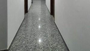 A hallway with white walls, granite flooring, and wooden doors. - Hotel Nue-Nest (Rishikesh)