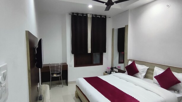 A bedroom with a bed, a desk, a chair, a ceiling fan, and a window with curtains. - Hotel Nue-Nest (Rishikesh)