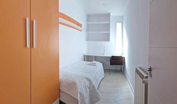 A bedroom with a bed, a desk, and a radiator.