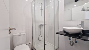 Un baño moderno con ducha de vidrio, inodoro blanco y lavabo negro con recipiente blanco.