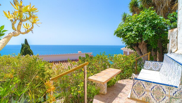 A stone staircase with a bench, leading to a terrace overlooking the sea.