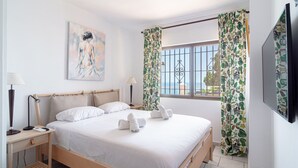 A bedroom with a bed, bedside tables, a lamp, a painting, and curtains.