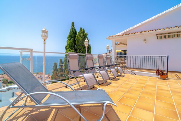 Una terraza con sillones de sol y vista al mar.