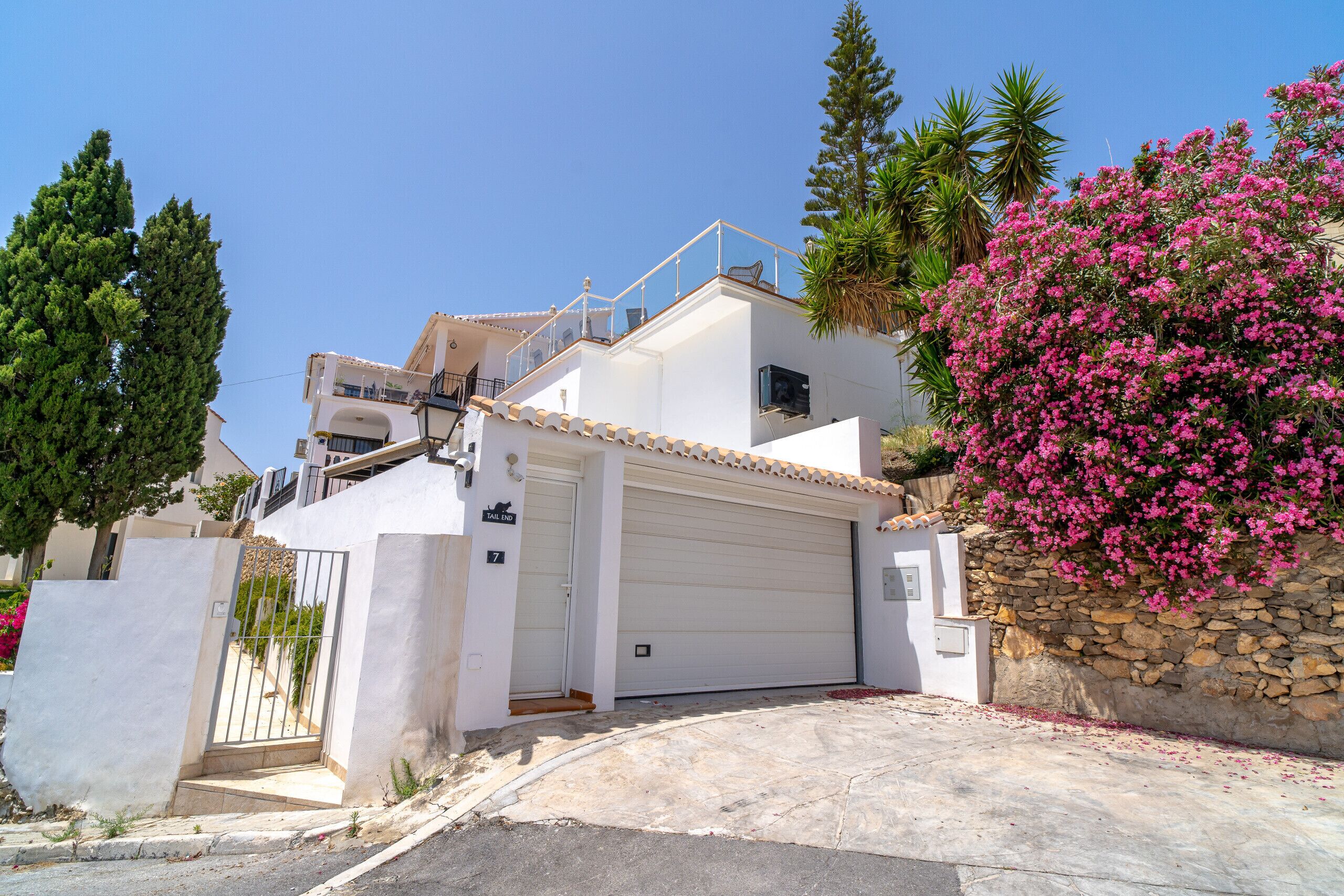 A two-story house with a white exterior, a garage, and a stone wall with pink flowers.