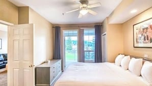 Habitación de hotel con una cama grande, ventilador de techo, escritorio y vistas al exterior a través de las ventanas.