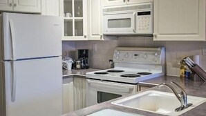 Una cocina con armarios blancos, un refrigerador, una estufa y un microondas.