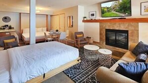 Una habitación de hotel con cama, sofá, televisión, chimenea y zona de comedor.