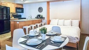 Una habitación de hotel compacta con kitchenette, comedor y cama.