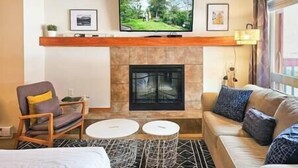 Una habitación de hotel con chimenea, un televisor colocado encima, un sofá, una silla y una pequeña mesa.