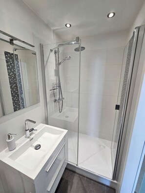 A modern bathroom with a glass-enclosed shower, a white sink, and a large mirror. - Herzlich Willkommen in der Wohnung 82 im Haus 3 der Vier Jahreszeiten (Großenbrode)