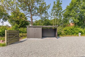 A small, enclosed outdoor structure with a metal door and a roof, surrounded by gravel and greenery. - Die Ferienwohnung "ellis Groot Stuuv" in Garding für bis zu 4 Personen (Garding)