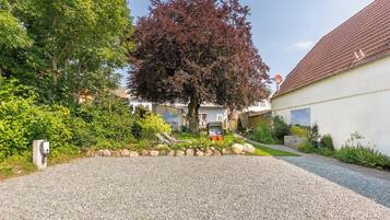 Ein Auffahrt mit Kiesbelag, ein Baum mit roten Blättern und ein Haus mit Ziegeldach.