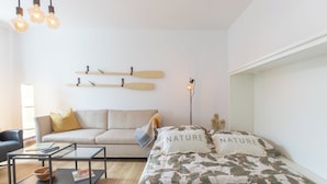 A modern living room with a sofa, a glass coffee table, and a bed with floral bedding. - Die Ferienwohnung "ellis Groot Stuuv" in Garding für bis zu 4 Personen (Garding)