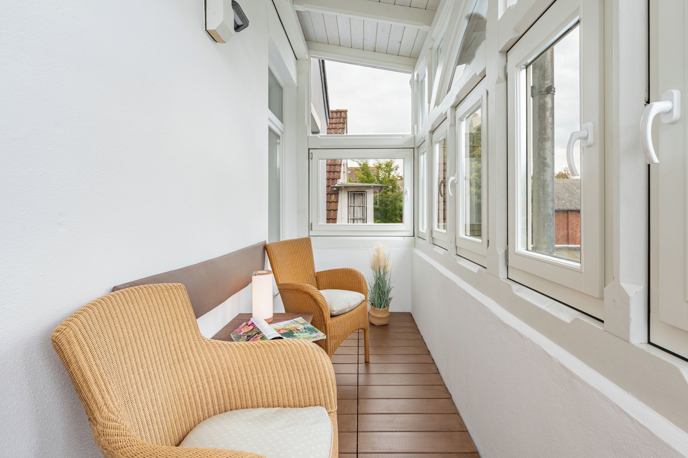 A covered balcony with wicker furniture, a lamp, and a potted plant.