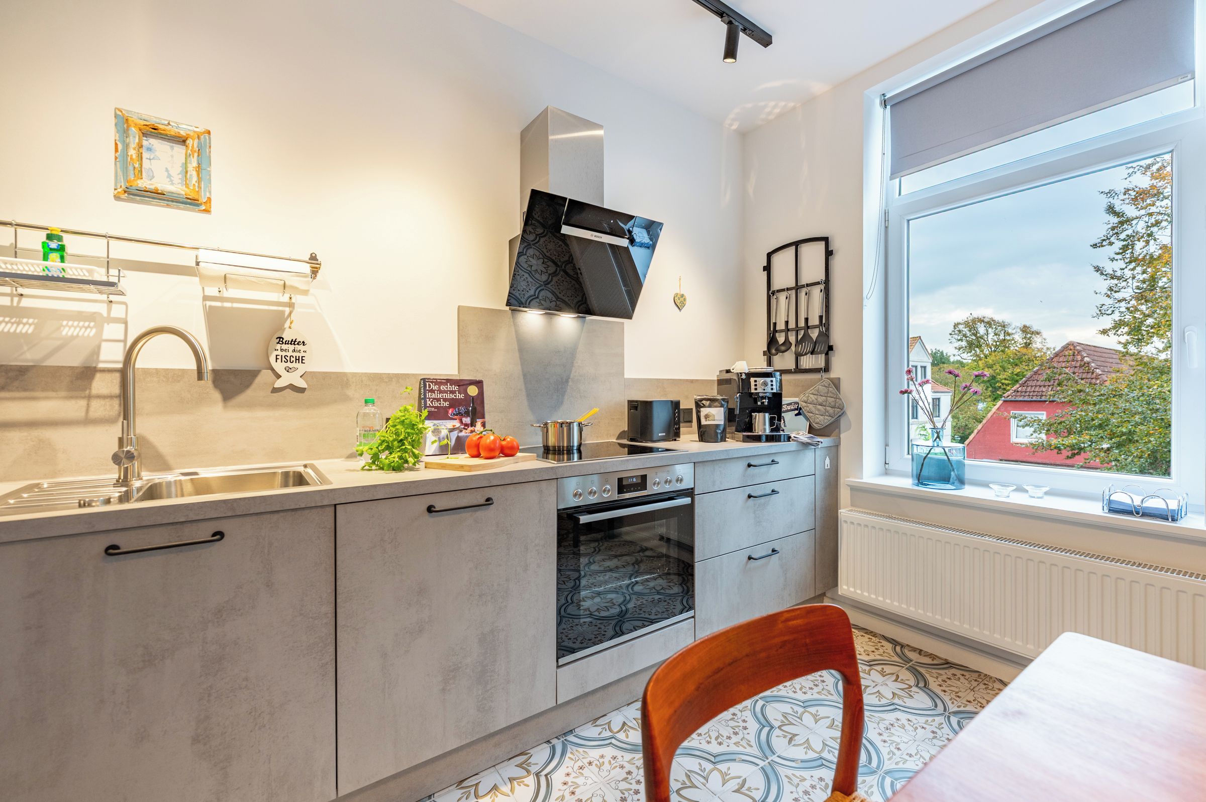 Eine moderne Küche mit Backofen, einer Kaffeemaschine und einem Fenster mit Blick auf ein Haus und Bäume.