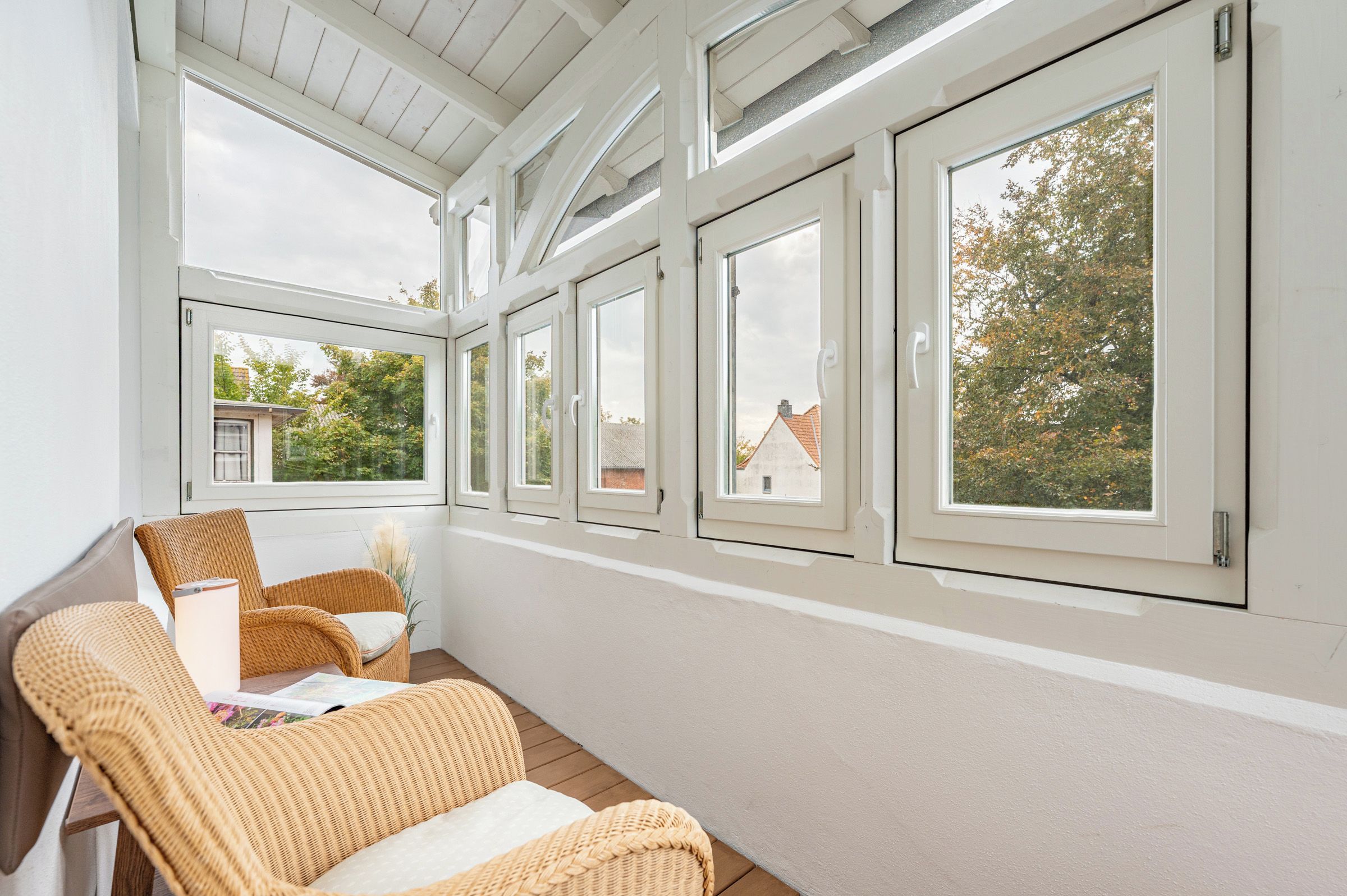 A sunlit room with a wooden floor, white walls, and a row of windows.