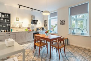 A modern kitchen with a dining area, featuring a large window, a hanging light fixture, and a variety of kitchen appliances.