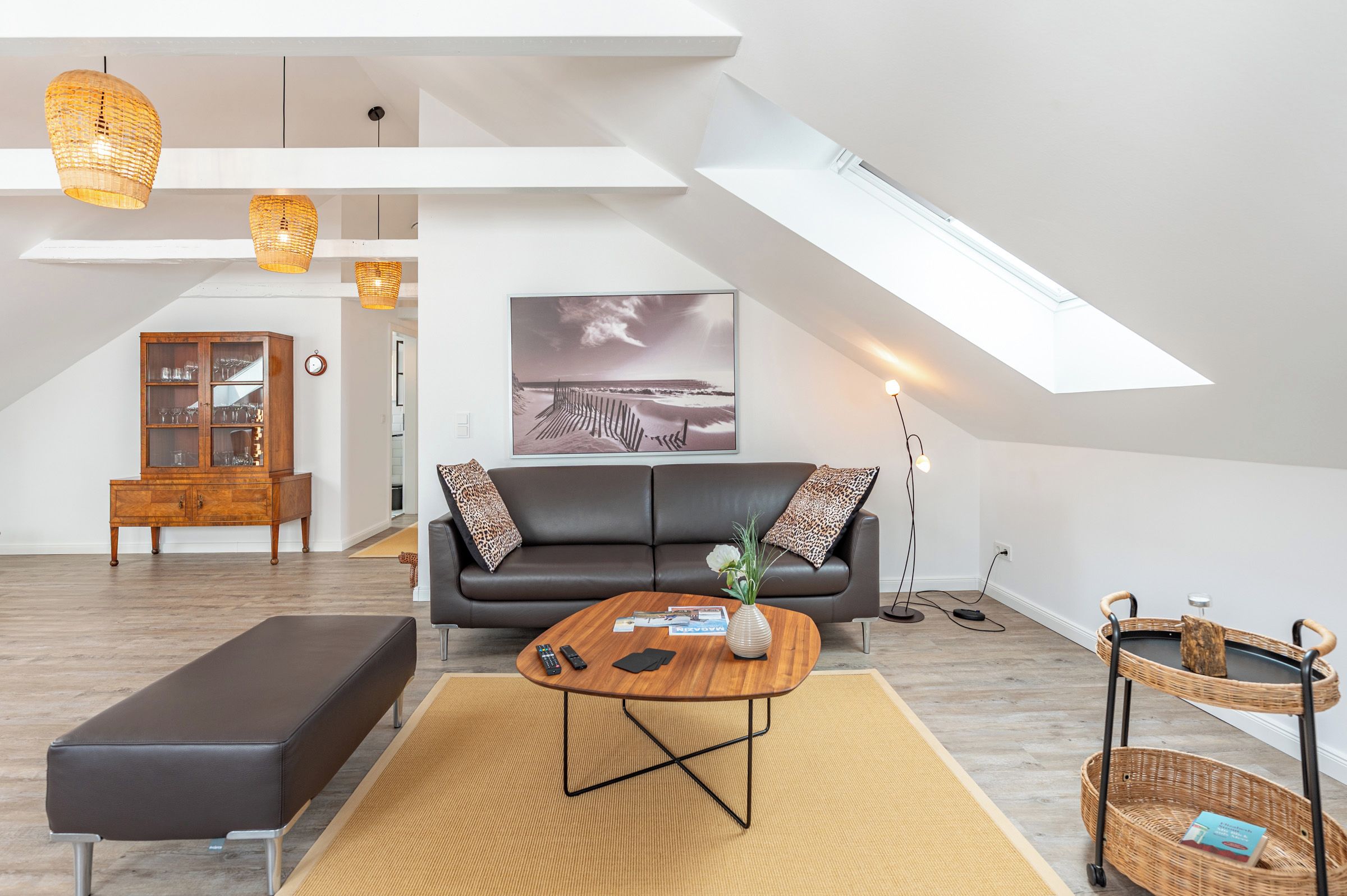 Ein modernes Loft mit hohen Decken, einem schwarzen Ledersofa, einem Holztisch und einem großen Fenster mit Blick auf eine Strandlandschaft.