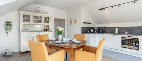 A modern kitchen with white cabinetry, a dining area with a wooden table and yellow chairs, and a ceiling light fixture.