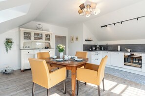 A modern kitchen with white cabinetry, a dining area with a wooden table and yellow chairs, and a ceiling light fixture.