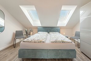 A bedroom with a large bed, two chairs, a bedside table, and a wardrobe. There are skylights above the bed. - Die Ferienwohnung "gretes Dackstuuv" in Garding für bis zu 4 Personen (Garding)