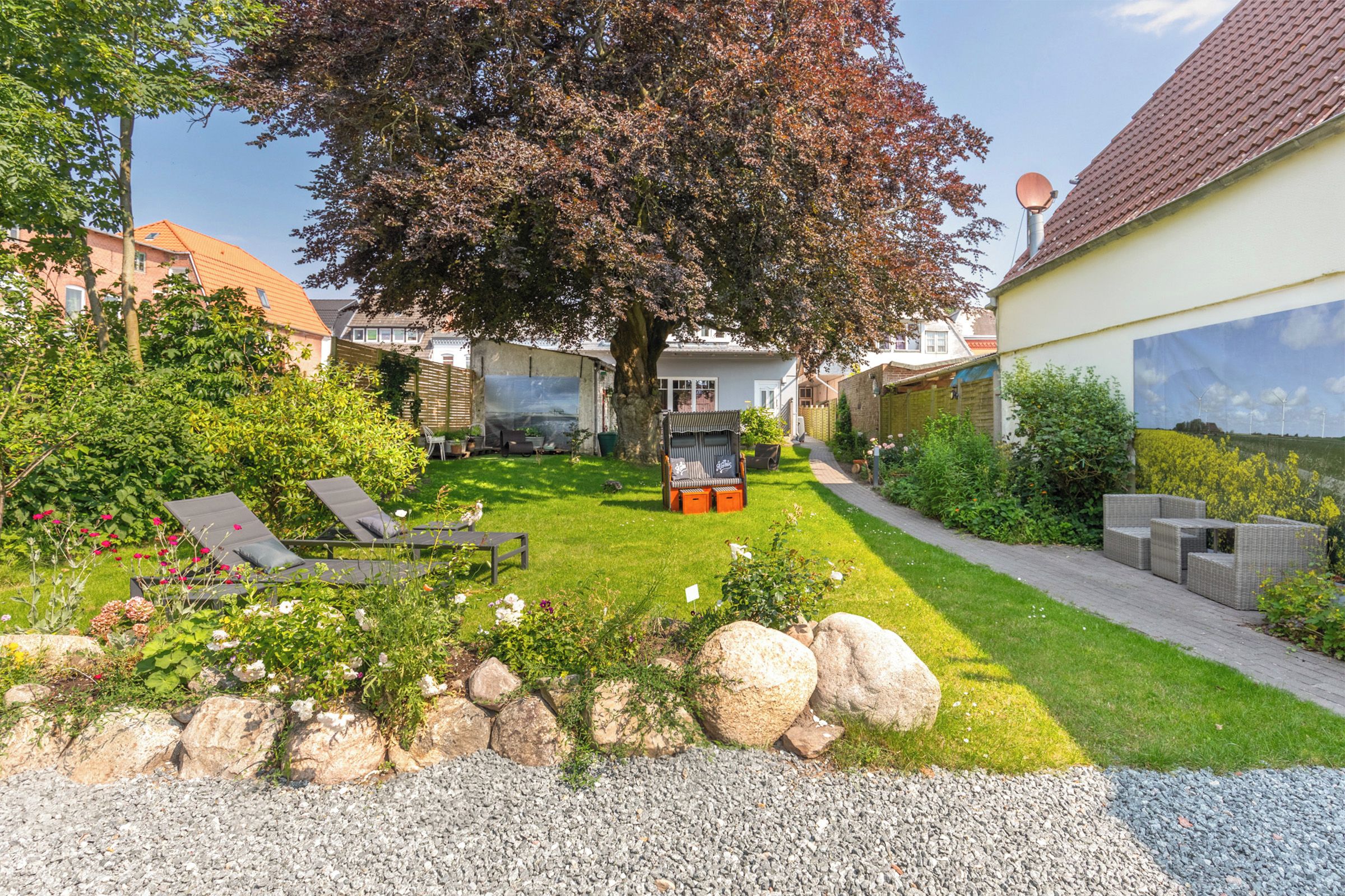 Een woon tuin met gazon, zitgedeelte en een grote boom.