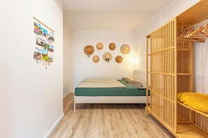 Une petite chambre à coucher accueillante, avec un lit, une armoire en bois et un mur décoré de chapeaux et de photos.