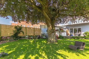 Ein Wohnhof mit einem großen Baum, einem Holzzaun, einer Rasenfläche und einem Haus mit einer Veranda.