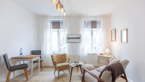 Een woonkamer met een houten eettafel, twee stoelen, een bank en een bijzettafeltje met een lamp.