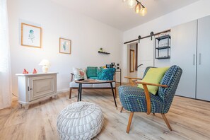 Un salon confortable avec un canapé, un fauteuil et un pouf, une petite table avec une lampe et un meuble.