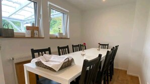 Comedor con una mesa blanca, sillas oscuras, ventanas amplias y un radiador.
