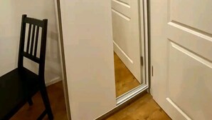 Una habitación con la puerta entreabierta, una silla de madera y un armario blanco.