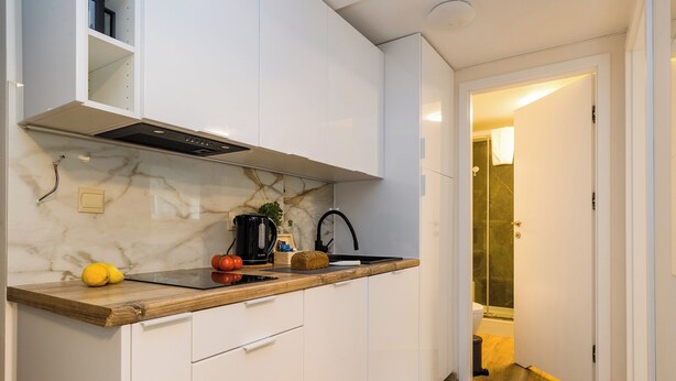 Una cocina moderna con armarios blancos, salpicadero de mármol y encimera de madera.