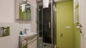 Un baño moderno con cabina de ducha de vidrio, un lavamanos blanco y una pared verde.