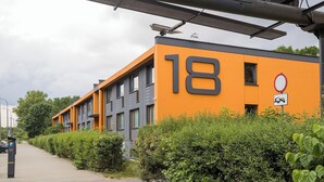 Un edificio moderno con el número 18 en su fachada, rodeado de vegetación.