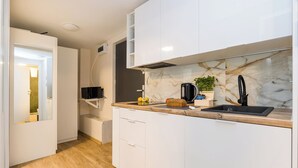 Una cocina moderna con armarios blancos, un salpicadero de mármol, un lavamanos negro y una encimera de madera.