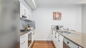 A modern kitchen with white cabinets, stainless steel appliances, and a wooden floor.