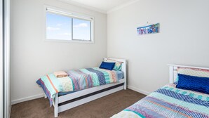 A bedroom with two single beds, a window, a ceiling fan, and a wall-mounted artwork.