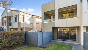 A modern two-story residential building with a flat roof, large windows, and a balcony.