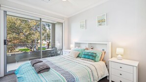 A bedroom with a large bed, a bedside table, a window with a view of trees, and a ceiling light.