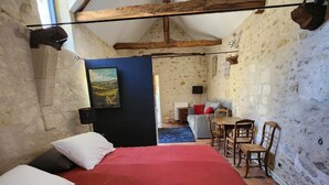 Ein rustikaler Raum mit einem Bett, Holzstühlen, einem kleinen Tisch und Blick ins Grüne durch ein Oberlicht.