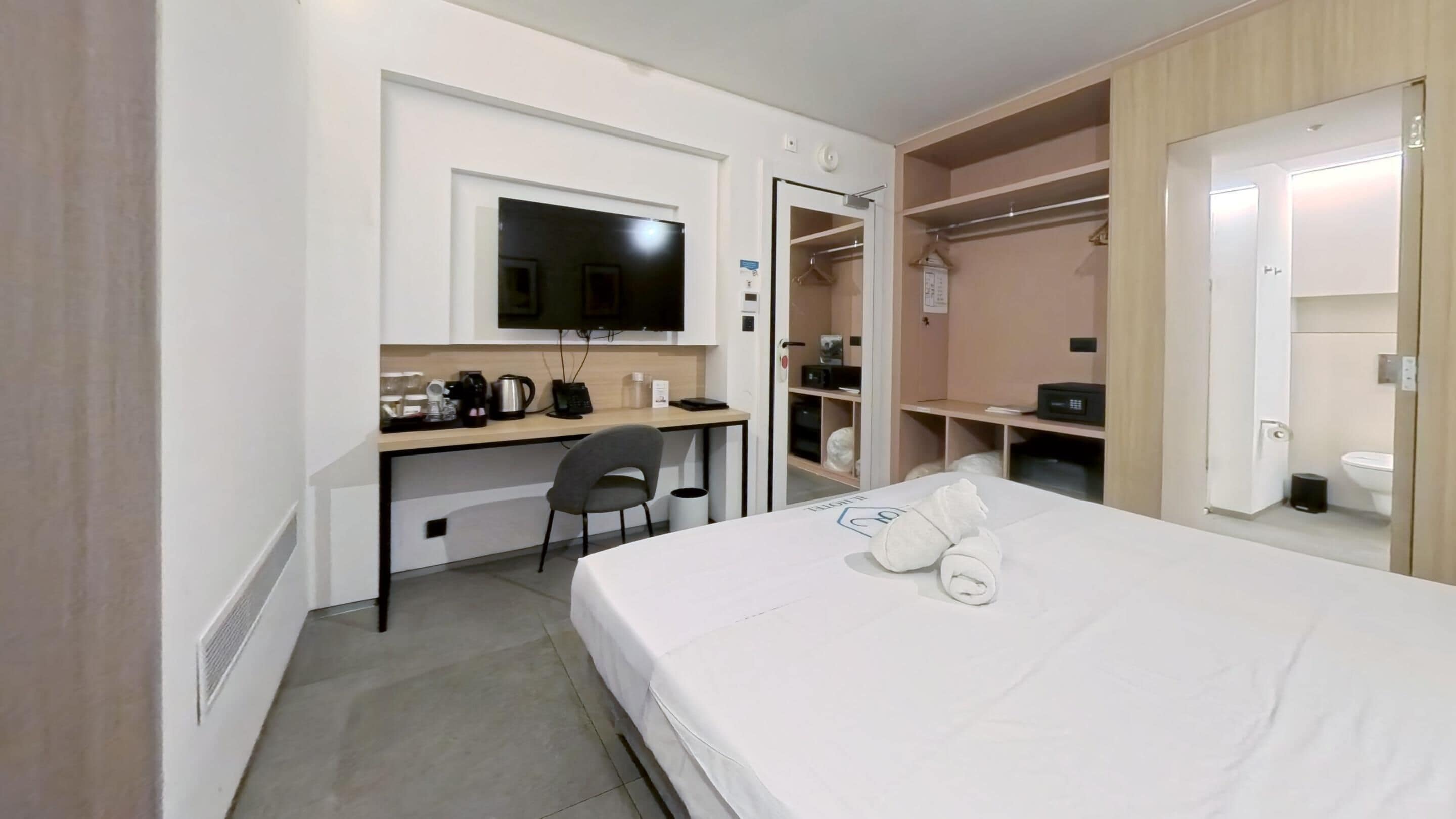 Et hotelværelse med seng, skrivebord, stol, fjernsyn, garderobeskab og badeværelse.